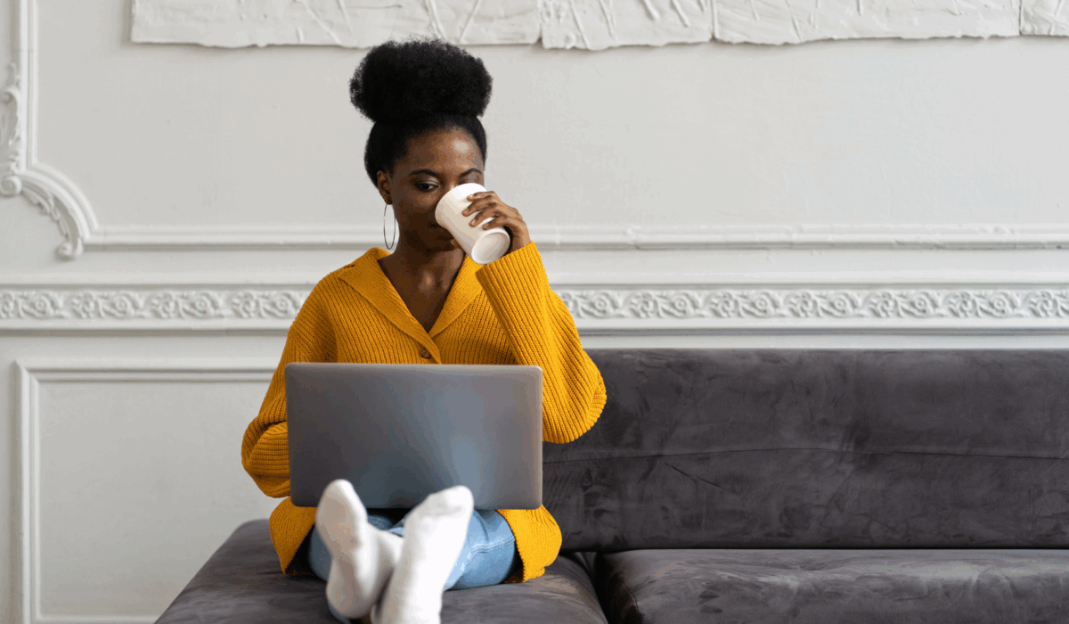 Woman in yellow sweater drinking coffee with legs outstretched.